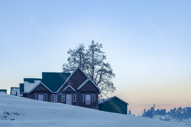 A stunning resort is visible amidst a snow-capped landscape, offering a slight glimpse of the majestic snow-capped mountains in the background in Gulmarg, Kashmir, India